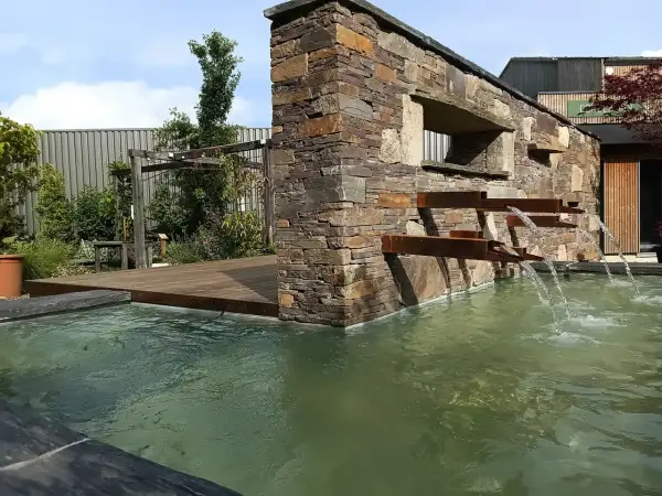 La mare aux plantes, avec sa cascade moderne en pierre et métal, invite à la détente. L'eau ruisselle doucement dans le bassin verdoyant.